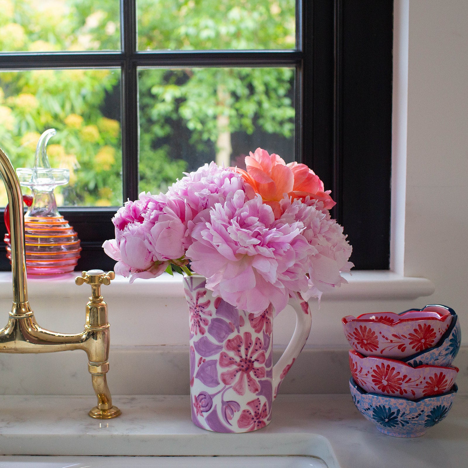 A vaisselle floral vase filled with flowers next two a sink and a stack of vaisselle candy b bowls in red a blue.
