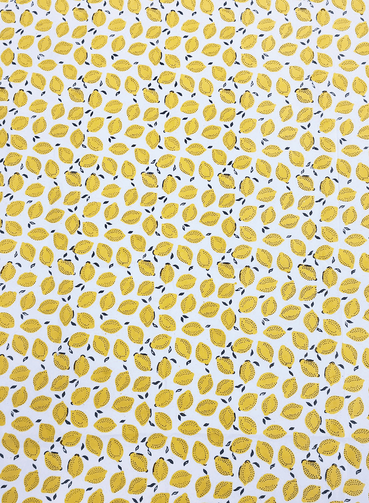A white cotton tablecloth decorated with yellow lemons and small black leaves.