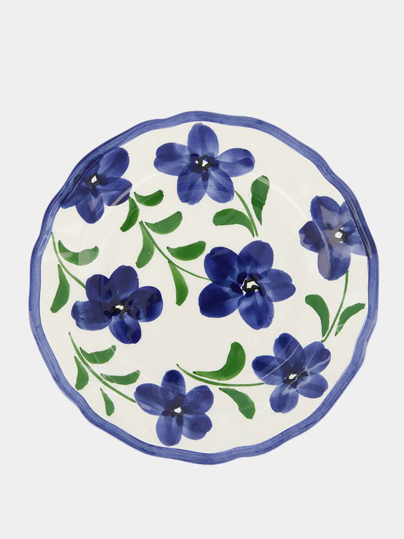 A ceramic round plate that is decorated with handpainted blue flowers and finished with a blue rim.