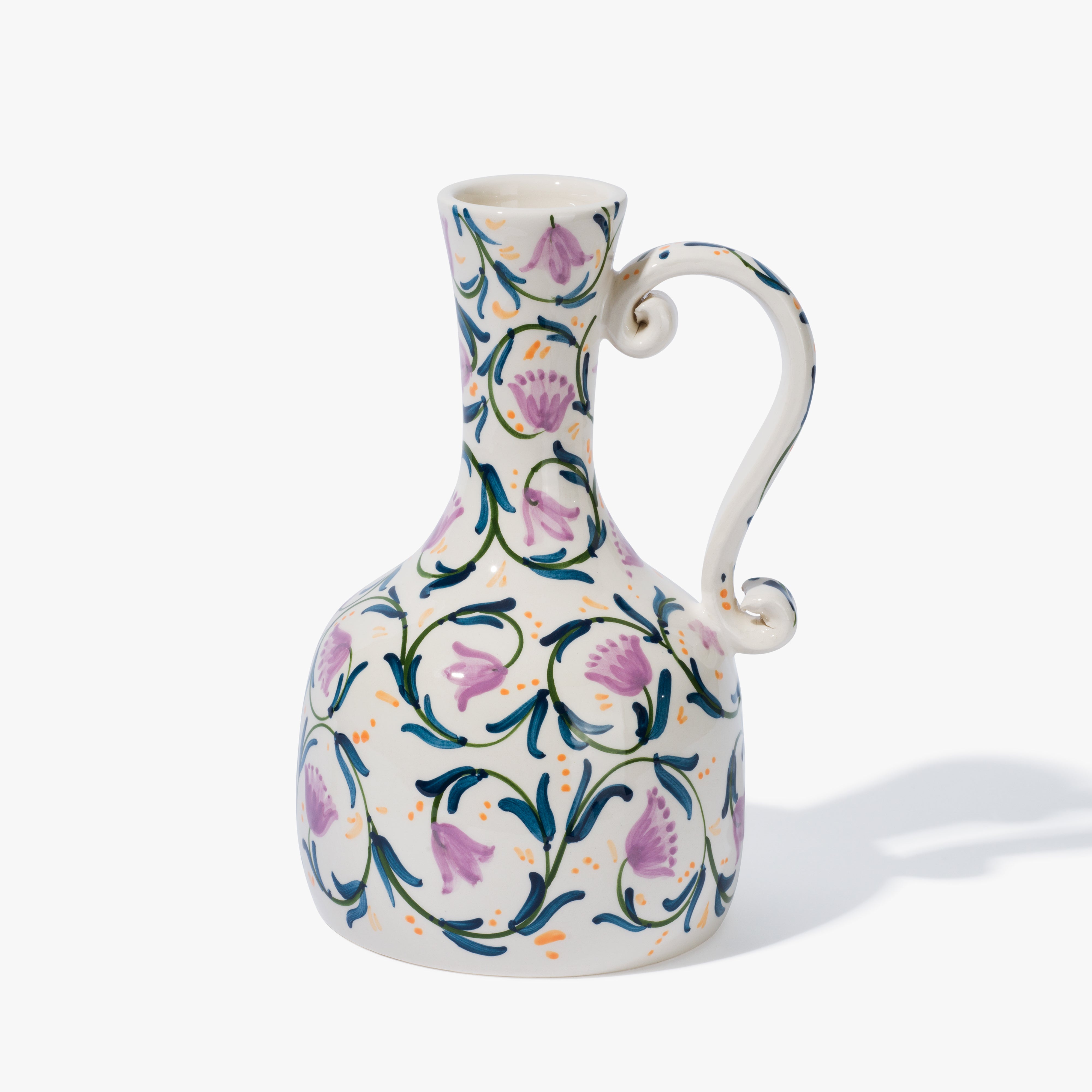 An ornate ceramic Vaisselle vase with a handle that has a lilac, lavender and green floral pattern covering it.