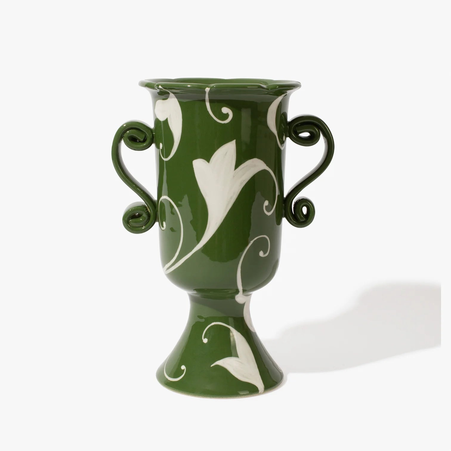Tall forest green coloured vase in an urn shape with two ornate handles. It has a white floral pattern painted on the vase and the top of the case has ascalloped edge. 