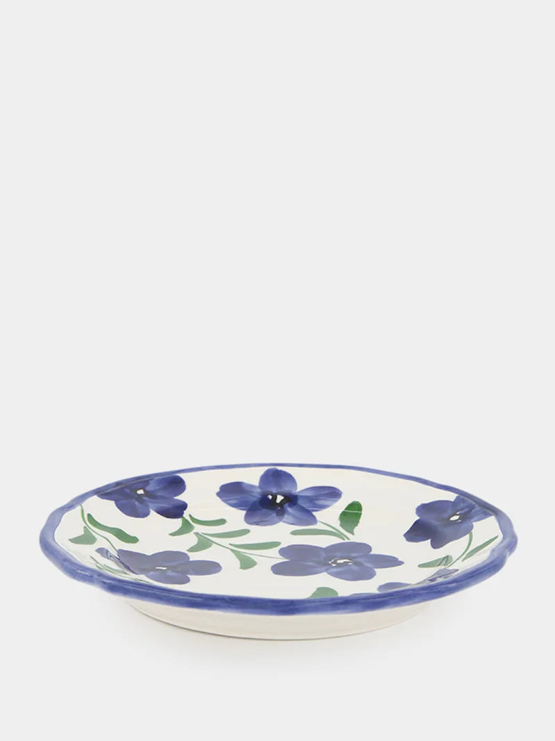 A ceramic round plate that is decorated with handpainted blue flowers and finished with a blue rim.