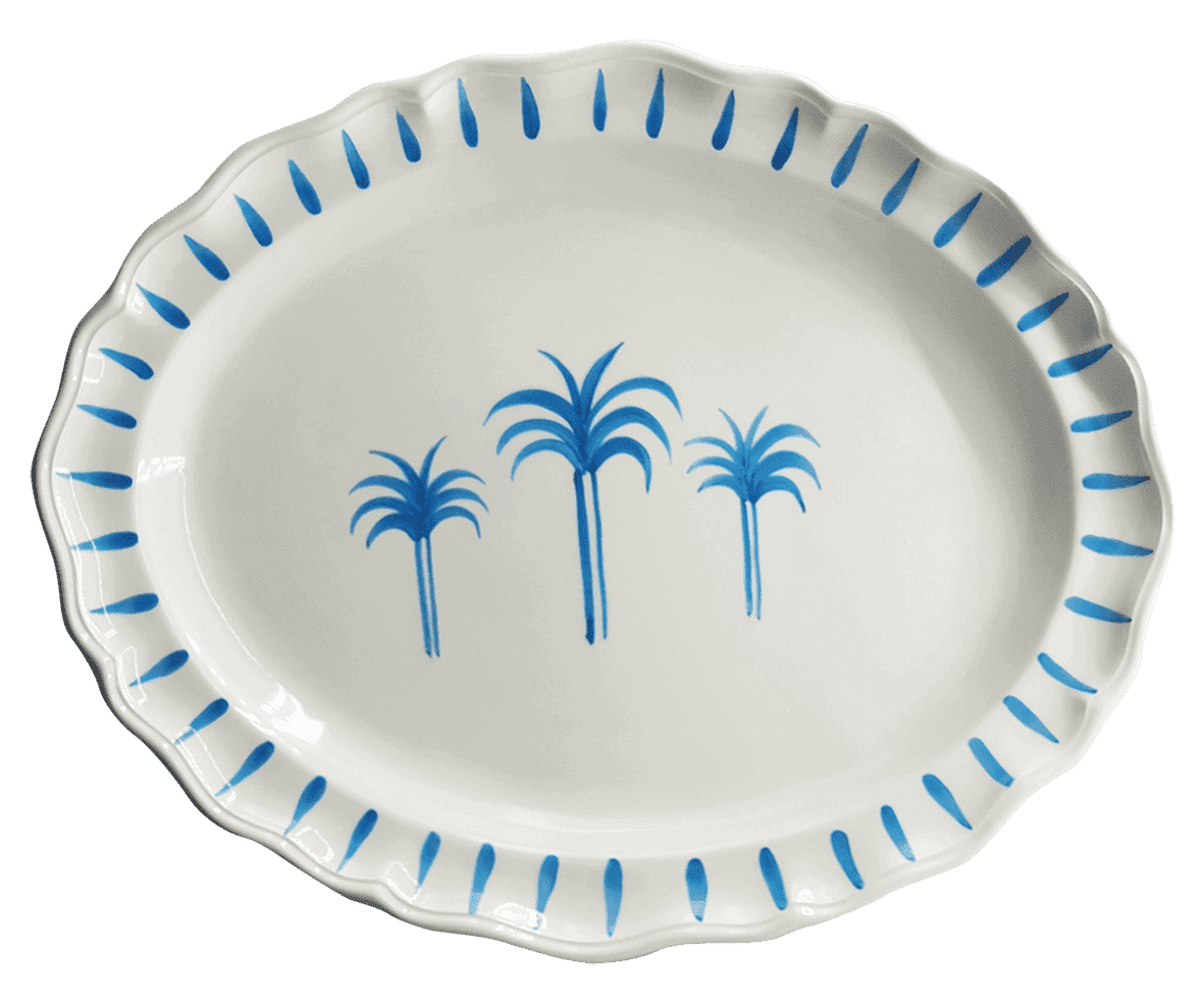 An oval ceramic plate with three palm trees painted in the centre in a bring blue. The rim is bright blue  lines that form an elegant border..