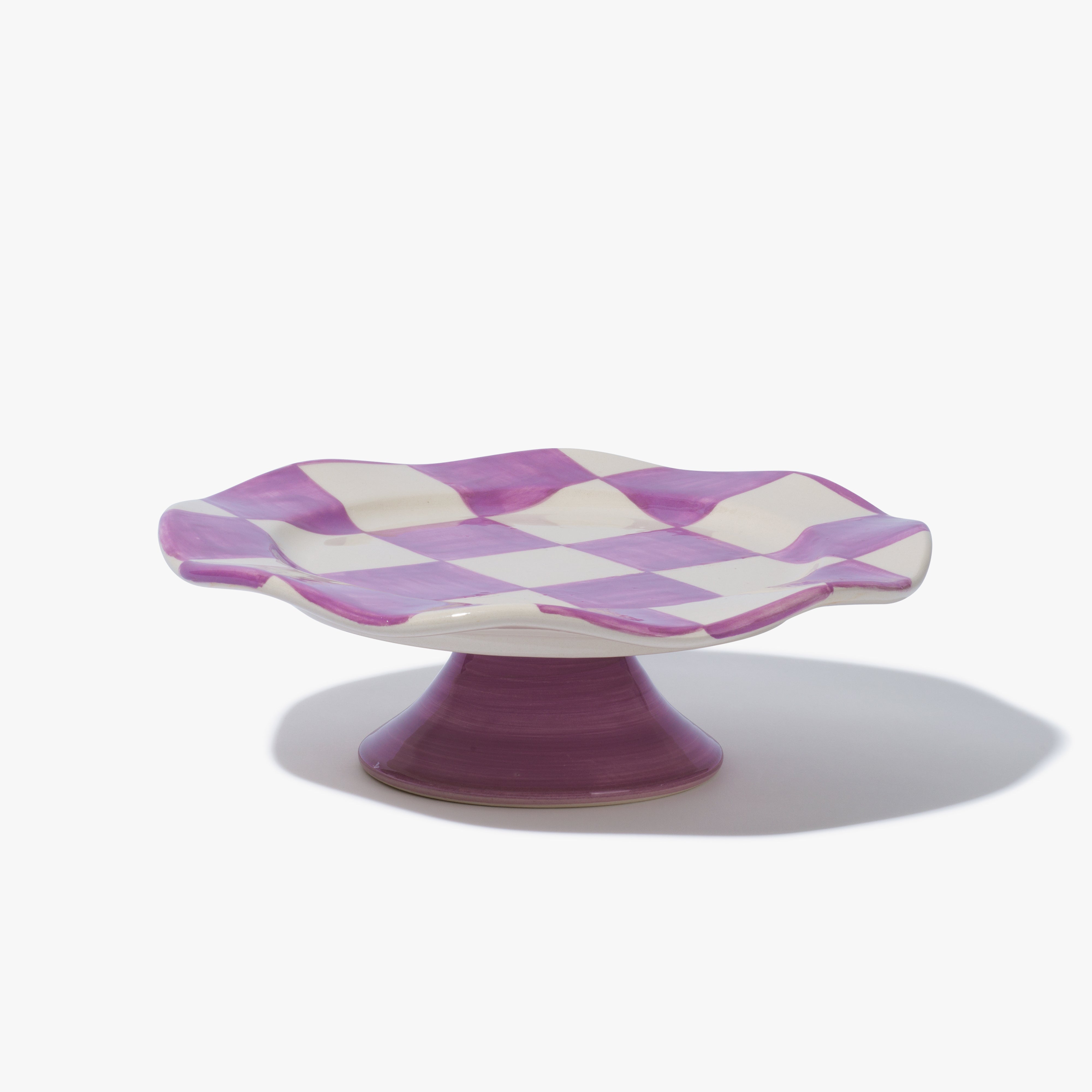 A cake stand with a purcple and white check pattern on the top and a purple base. It has a fluted/ scalloped rim. 