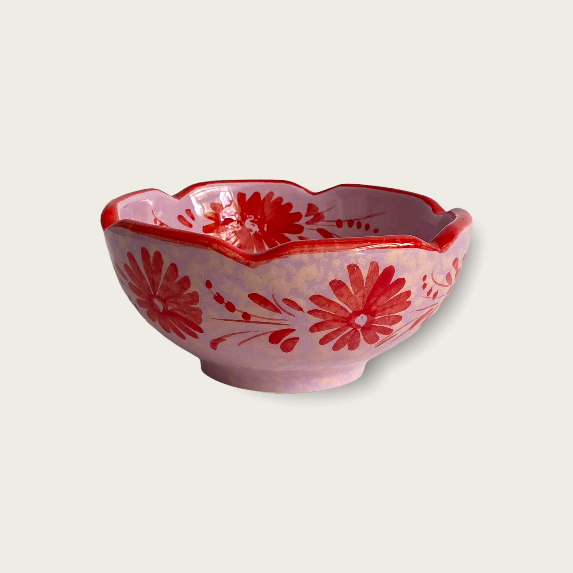 A cute handpainted ceramic bowl that is predominately lilac with red flowers, a red scalloped rim and a light speckled pattern.