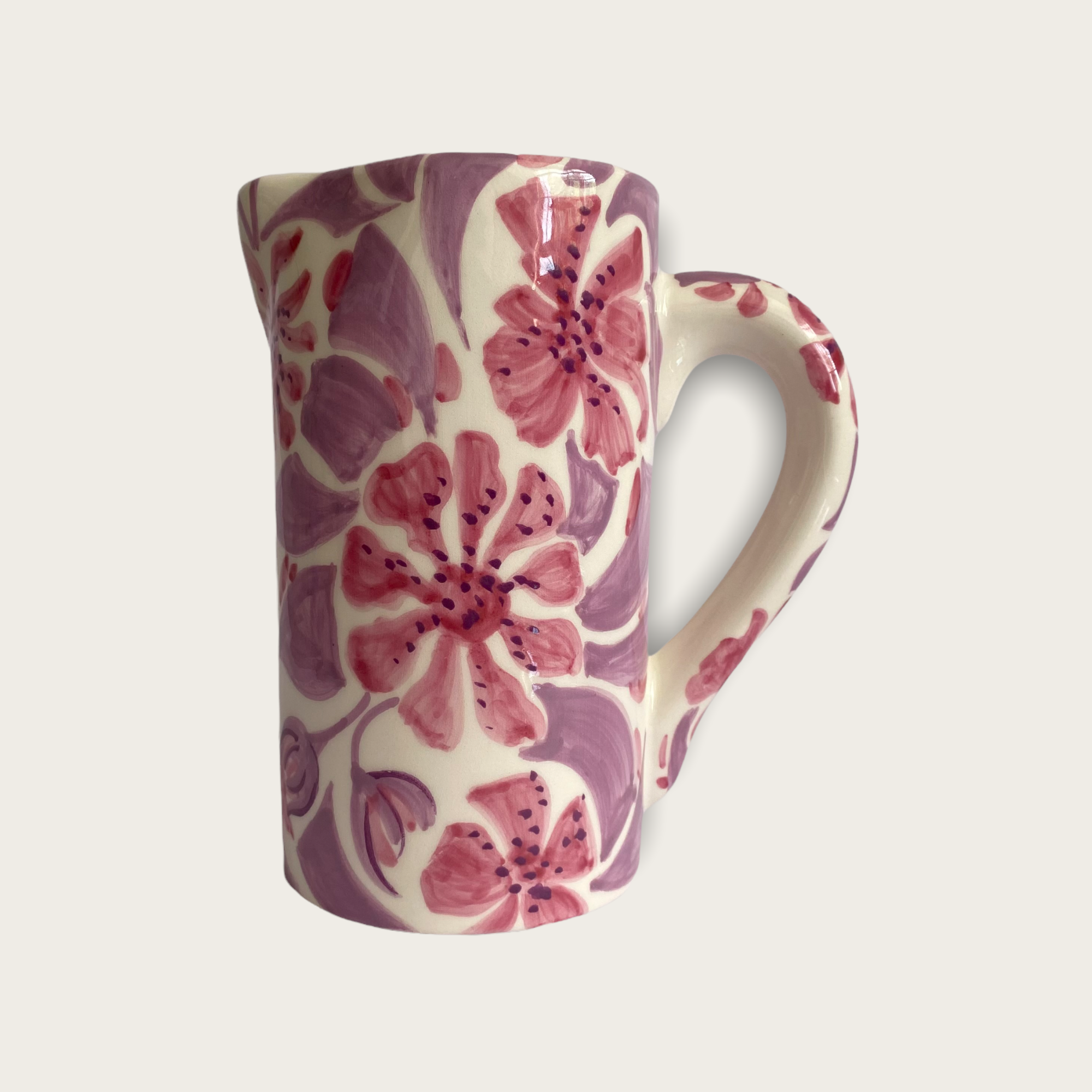A ceramin jug or vase the has a spout and a handle. It is white with pink flowers and a lilac coloured pattern around the flowers. 