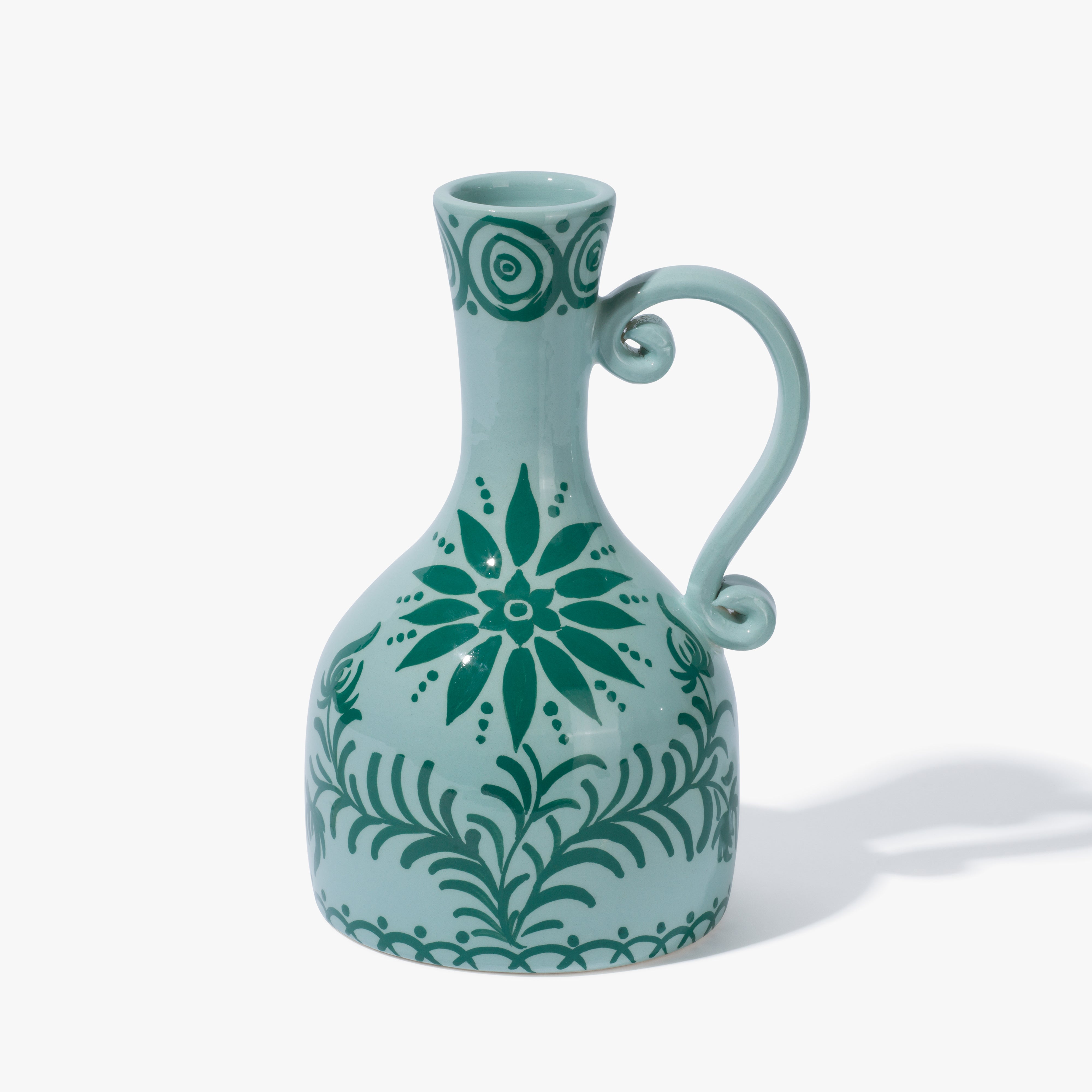 A Vaisselle ceramic vase witha handle. The vase is light blue and contains a decorative pattern in forest/ pine green.